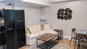 A modern living room with a black refrigerator, beige sofa, wooden coffee table, and a wall art piece.
