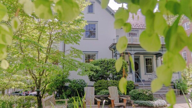 A two-story house with a porch, surrounded by greenery and a small garden.