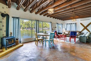 Una habitación con un ventanal grande, vigas de madera, chimenea y un comedor con sillas y una mesa.