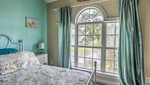 A bedroom with a bed, a nightstand, a lamp, and a window with curtains. - Lovely Myrtle Beach Condo: 4 Mi to Boardwalk! (Myrtle Beach)