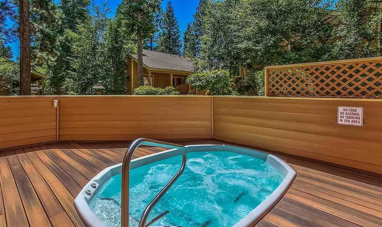 Un bain à remous doté d’une terrasse en bois, entouré d’arbres et délimité par une clôture en bois.