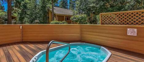 A hot tub with a wooden deck, surrounded by trees and a wooden fence.