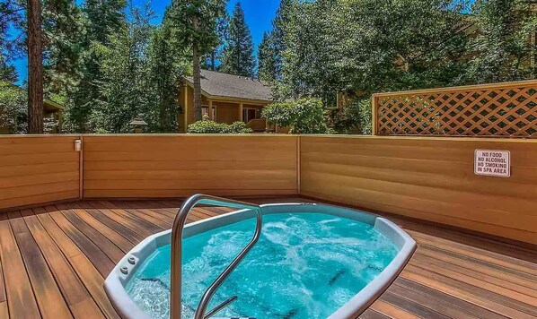 Un jacuzzi con terraza de madera, rodeado de árboles y una valla de madera.