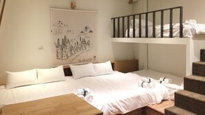 Une chambre avec un lit superposé, un lit recouvert de draps blancs, une table de chevet en bois et un mur orné d’une œuvre d’art représentant un paysage de montagne.