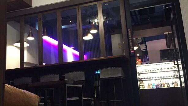 Un espace bar doté d’un plancher en bois, d’un coin salon et offrant une vue sur le bar grâce à de grandes fenêtres.
