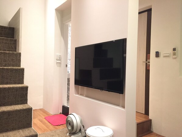 A staircase leading to a landing with a flat-screen TV mounted on the wall, a small fan, and a trash bin.