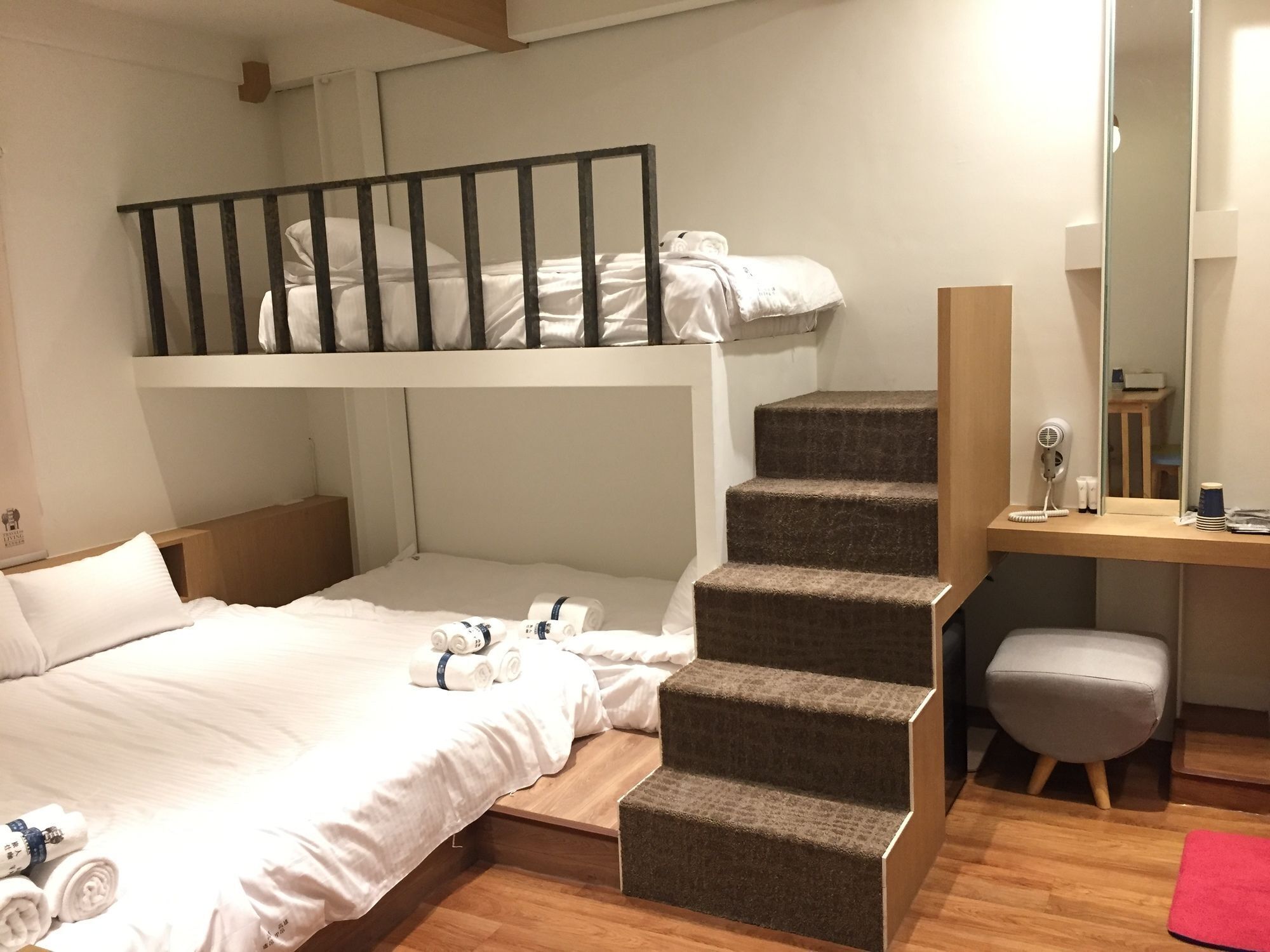 A bunk bed room with a desk and chair, a mirror, and a small stool.