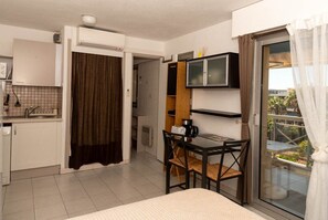 Ein kompaktes Hotelzimmer mit Küchenzeile, Essbereich, Bett und einer Schiebetür zum Balkon.