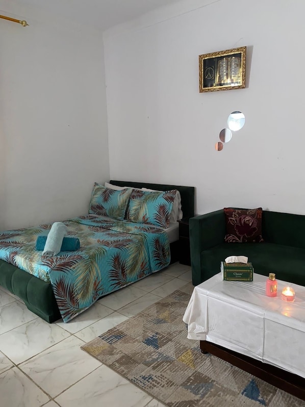 A room with a bed, a green sofa, a small table with a tissue box and a candle, and a wall-mounted picture frame.