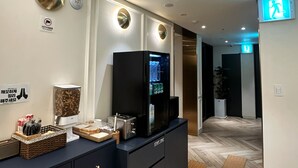 Una moderna zona de recepción de hotel con un mostrador azul oscuro, una pantalla digital y un dispensador de agua.