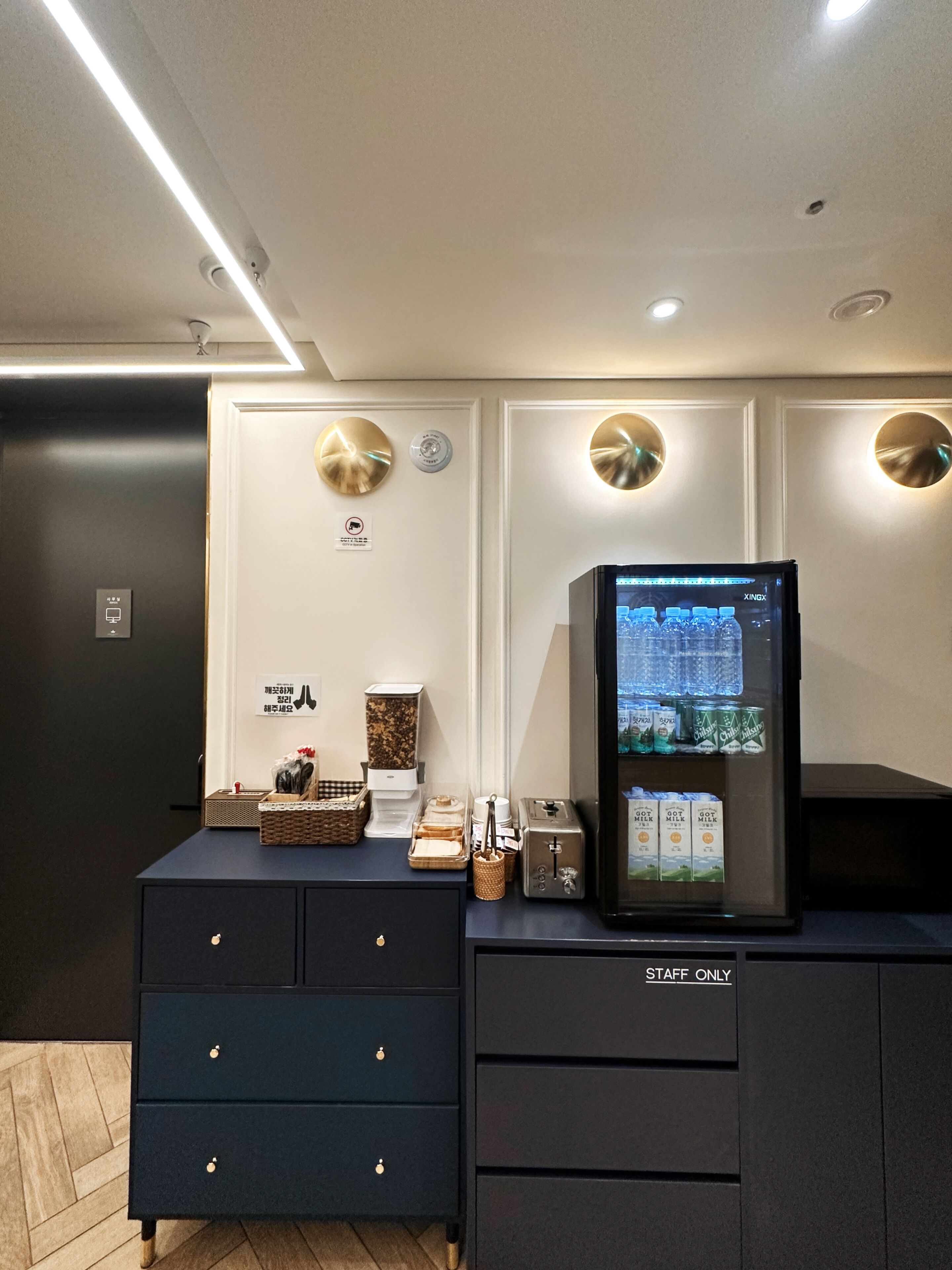 Habitación de hotel moderna con minibar, máquina de café y refrigerador lleno de bebidas.