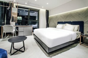 A modern hotel room with a large bed, a desk, a chair, and a small table.