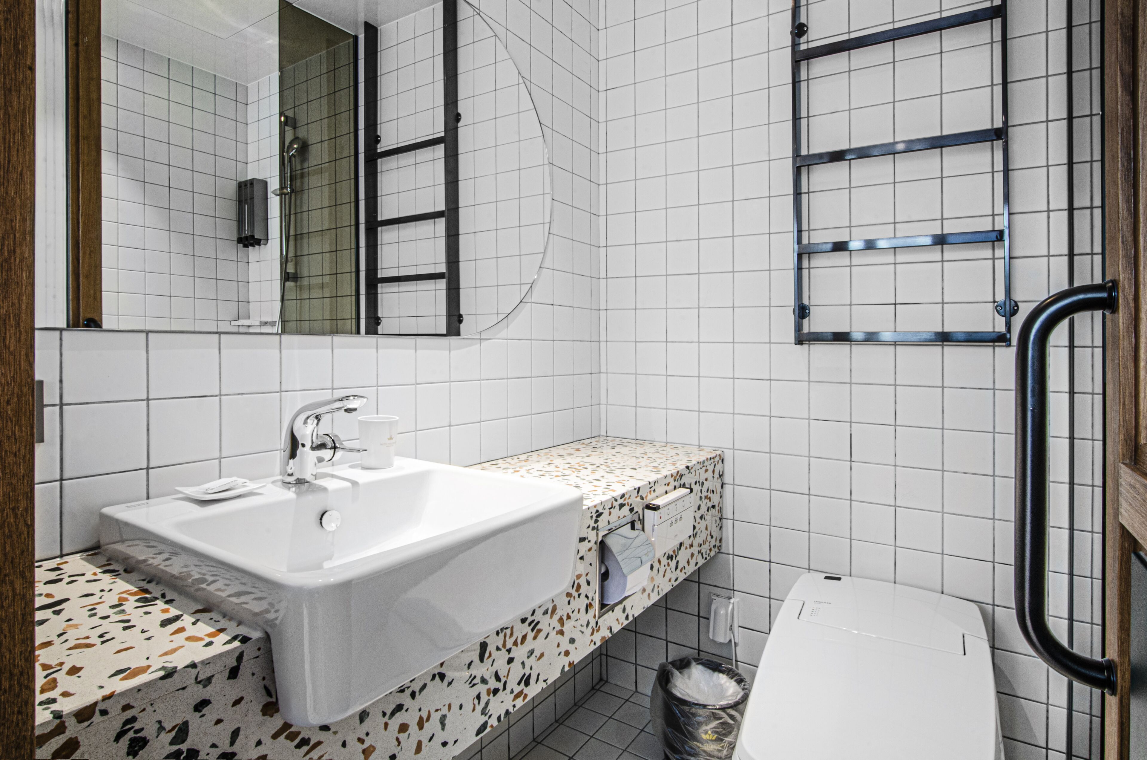 Un bagno con lavandino bianco, specchio, doccia e porta asciugamani.