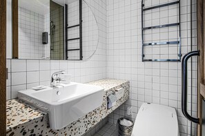 A bathroom with a white sink, a mirror, a shower, and a towel rack.