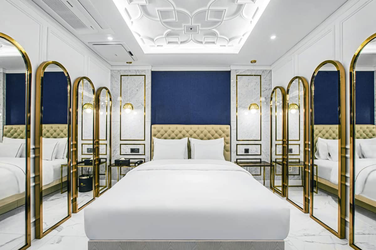 Une chambre d’hôtel luxueuse, dotée d’un grand lit, d’une armoire avec des portes miroir et d’un design moderne au niveau du plafond.