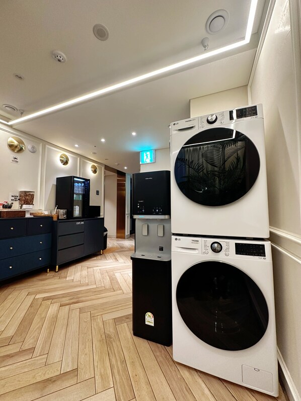 A modern laundry room with a stacked washer and dryer, a water dispenser, and a blue cabinet with drawers.