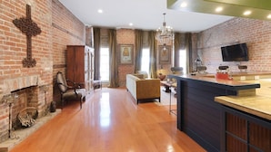 Un salón amplio con pared de ladrillo, chimenea y una moderna zona de cocina.
