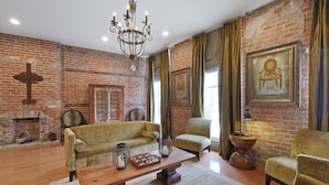 Una habitación con pared de ladrillo, candelabro, sofá, sillón, mesa y chimenea.