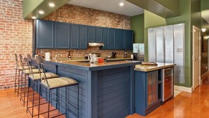 Una cocina con una isla central, armarios azules y una pared de ladrillo decorativa.