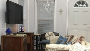 Een woonkamer met houten vloer, een televisie aan de muur, een houten kast, een blauwe stoel en een deur met raam.