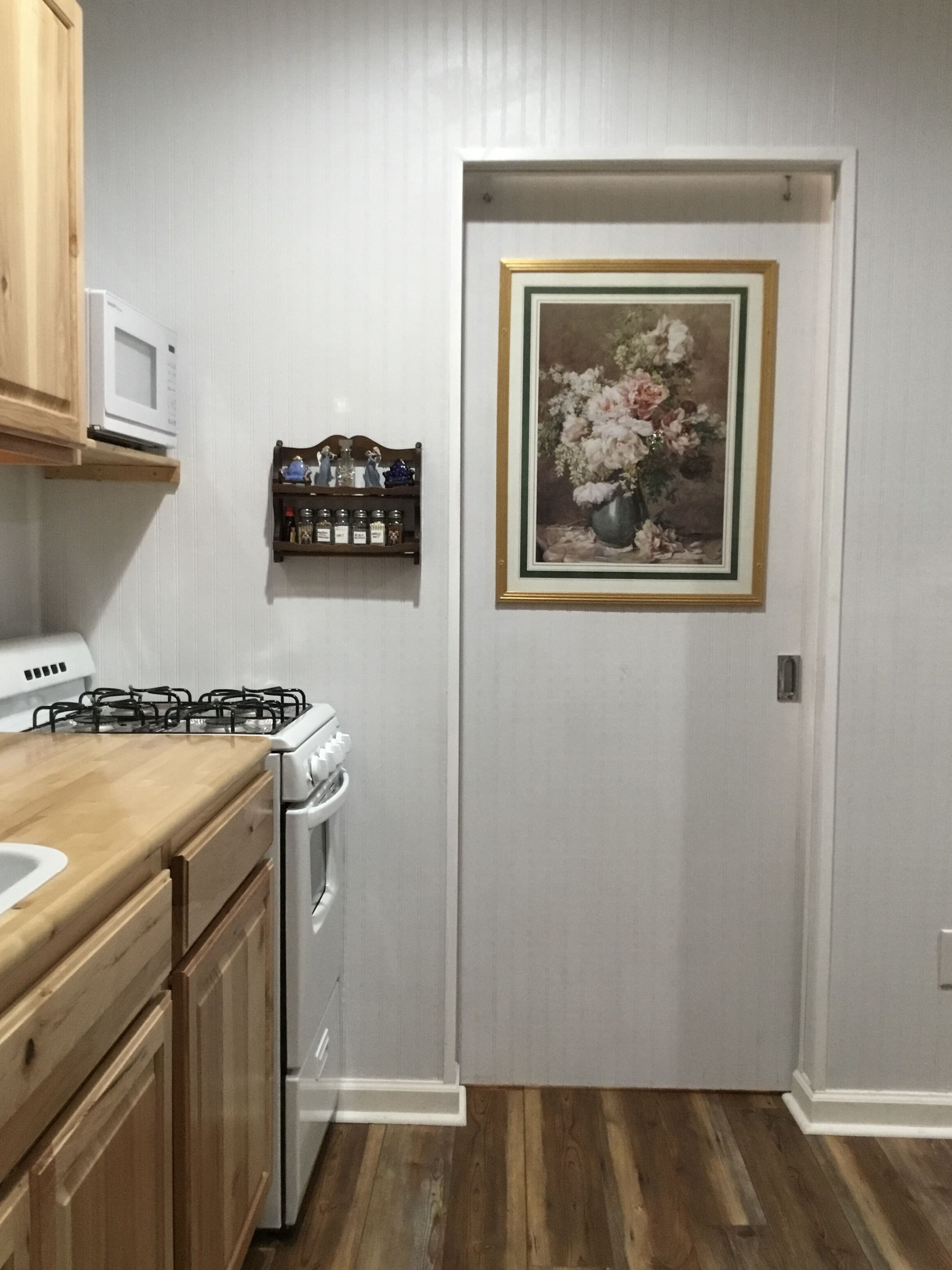 A kitchen with wooden cabinets, a microwave, a gas stove, and a white oven. There is a framed painting of flowers on the wall.