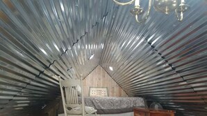 Een knus zolderkamer met schuine wanden, een schommelstoel, een bed en een houten dressoir.