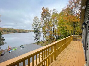Une terrasse en bois avec une balustrade donnant sur un lac, entourée d’arbres aux feuilles d’automne.