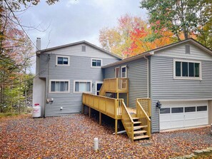 A two-story house with a wooden staircase leading to a balcony, a garage, and a gas can outside. - Spacious Pocono Lakefront Retreat w/ Amenities (pocono lake)