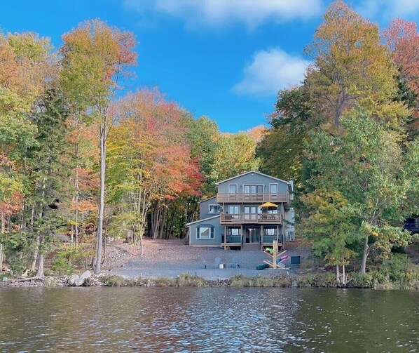 A two-story cabin with a balcony, surrounded by autumn-colored trees and a body of water. - Spacious Pocono Lakefront Retreat w/ Amenities (pocono lake)