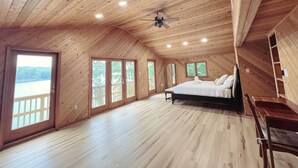 Un espacioso dormitorio con techo de madera, una cama, ventilador de techo y amplias ventanas con vistas al exterior.