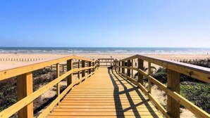 Un paseo marítimo de madera que conduce a una playa con cielos despejados.