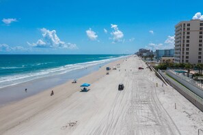 A wide beach with a clear sky, a few umbrellas, and a road parallel to the beach.
