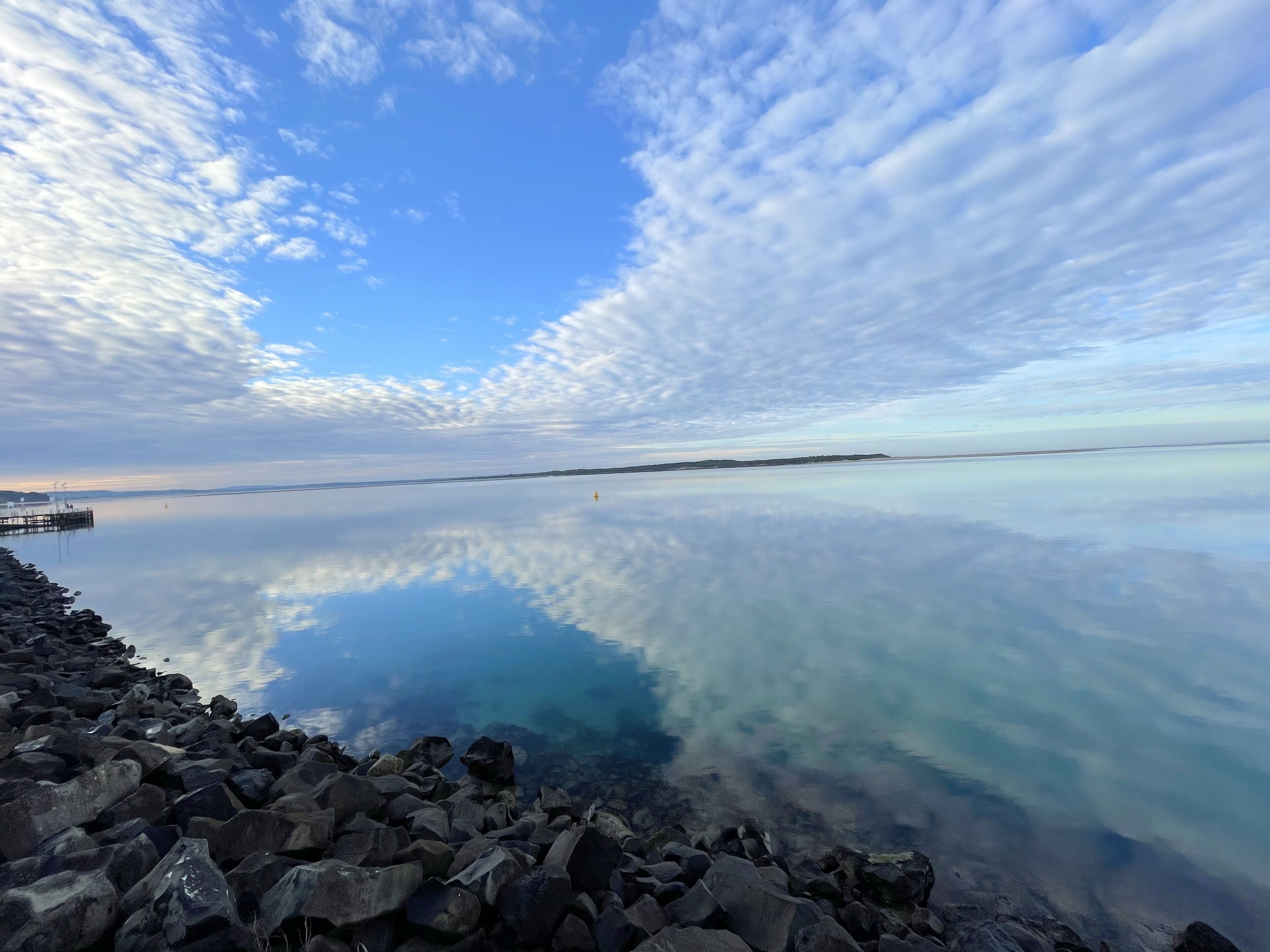 Un lac paisible, bordé d’une rive rocheuse, avec une jetée qui s’avance dans l’eau.