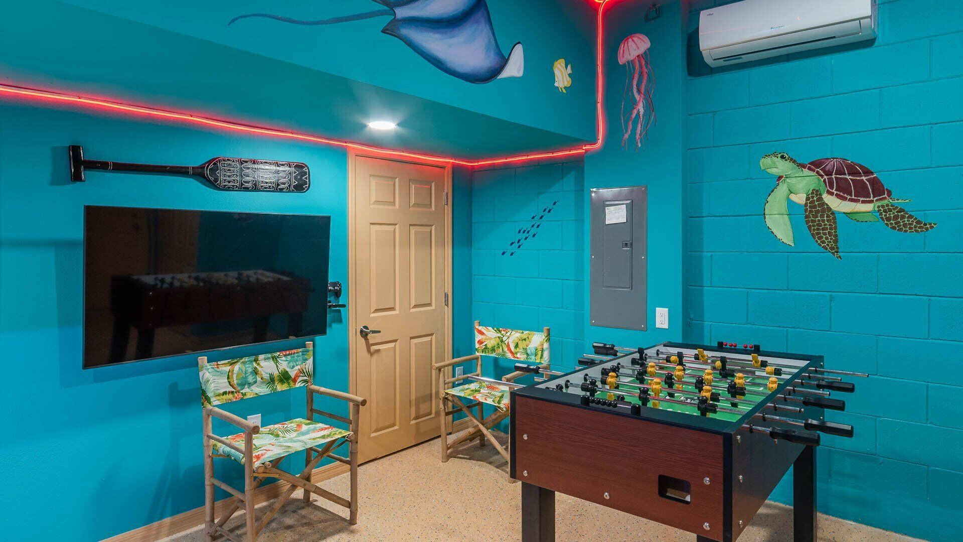 A room with a foosball table, two chairs, a TV, and a door.