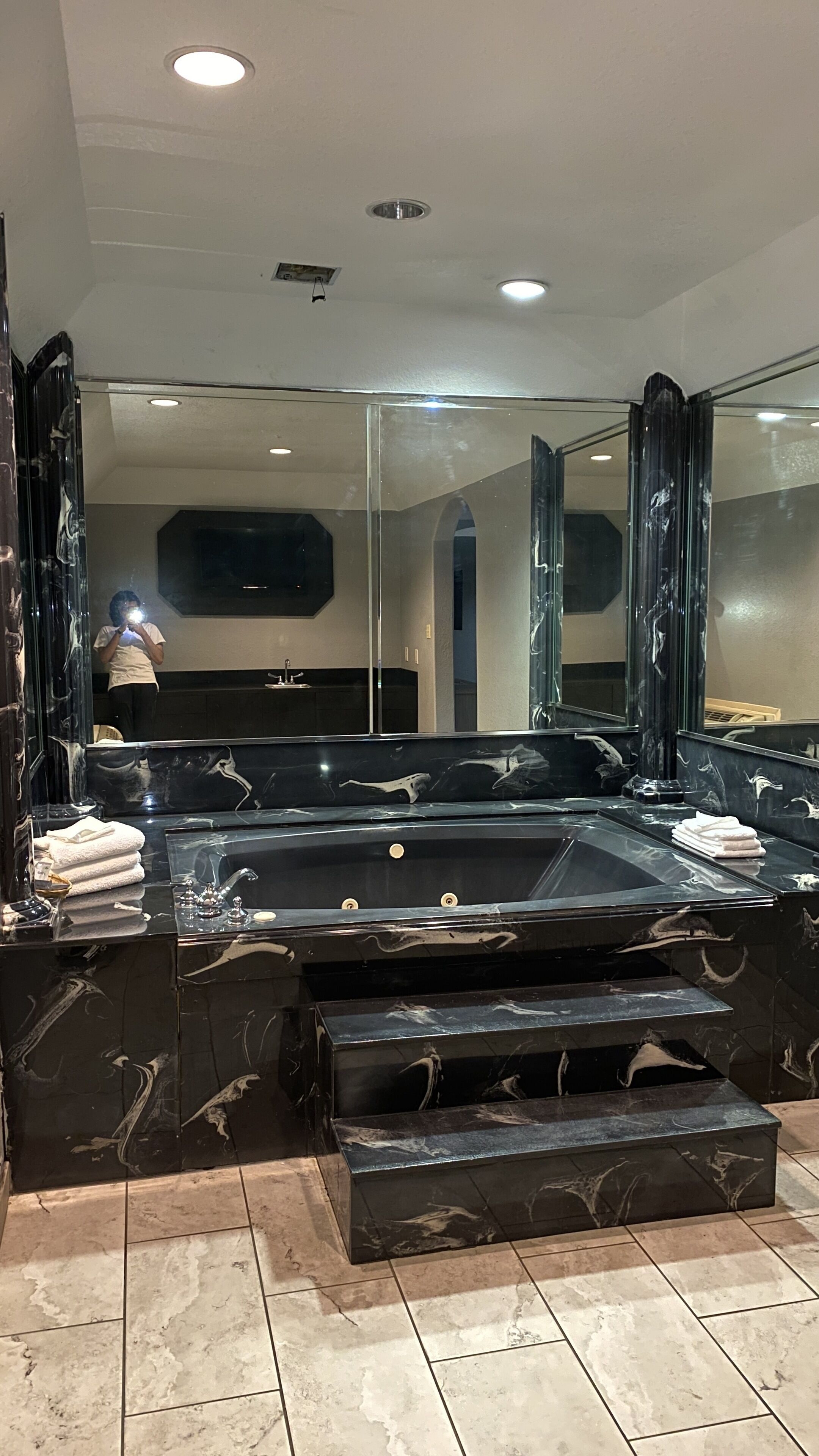 A modern bathroom with a large marble sink, multiple mirrors, and a bathtub.