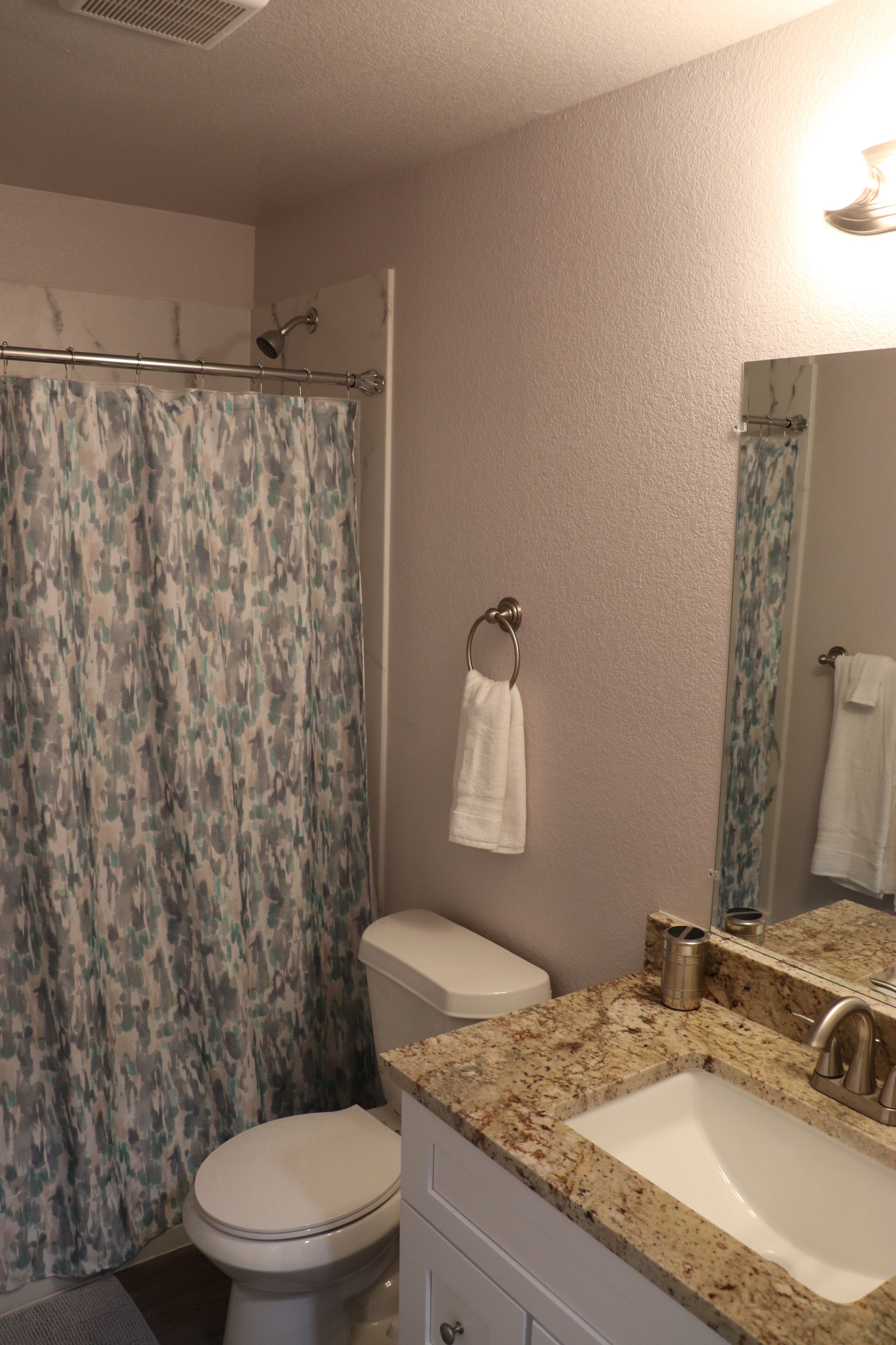 A bathroom with a shower curtain, toilet, sink, and a mirror.