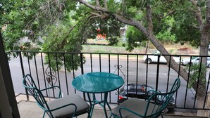 Ein Balkon mit zwei Stühlen und einem Tisch, der auf eine Straße mit parkenden Autos und Bäumen blickt.