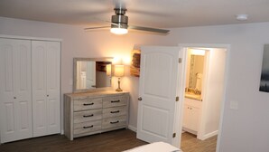 Ein Schlafzimmer mit einem Bett, einer Kommode, einem Deckenventilator und einer Tür zu einem Badezimmer.