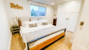 A bedroom with a wooden bed frame, white bedding, a bedside lamp, a window with a view, and a 'Relax' sign on the wall. - Farmhouse by the Falls (Snoqualmie)