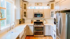 A modern kitchen with stainless steel appliances, white cabinetry, and a large window providing natural light. - Farmhouse by the Falls (Snoqualmie)