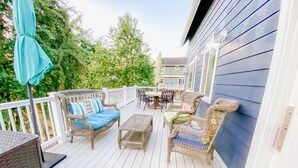 A covered outdoor deck with wicker furniture, a table, and chairs. - Farmhouse by the Falls (Snoqualmie)