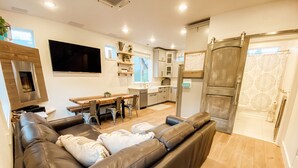 A modern living room with a leather sofa, a flat-screen TV, and a dining area with a wooden table and chairs. - Farmhouse by the Falls (Snoqualmie)