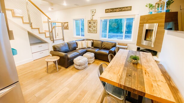 A modern kitchen with a wooden dining table, a black leather sofa, and a staircase leading to an upper level. - Farmhouse by the Falls (Snoqualmie)