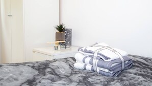 A neatly made bed with a marble-patterned bedspread, a bedside table with a potted plant, a candle, and a geometric-patterned box. - Large Shoreditch, Hoxton 3-Bed Garden Flat (London)