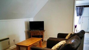 A living room with a sofa, a wooden table, and a television on a stand. - Nice big 2 double bedroom Apartment in the Town (Newquay)