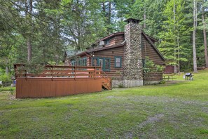 A rustic cabin with a stone chimney, wooden deck, and a picnic table in a forested area. - Steps to Lake: Tafton Cottage w/ Fire Pit & Grill (Tafton)