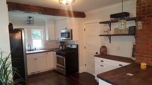 A kitchen with white cabinets, a stainless steel oven, a microwave, and a coffee maker. There are wooden shelves with jars and a small plant on the counter. - Very Welcoming (East Stroudsburg)