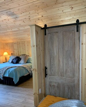 A wooden room with a bed, a wooden door, and a table. - Adorable Mountain Cabin near Asheville (Candler)