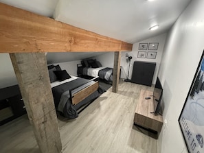 A compact room with two bunk beds, a standing fan, a small desk, and a framed welcome sign.