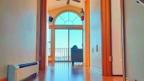 Un pasillo con piso de madera, un radiador y vista a un balcón con una silla.